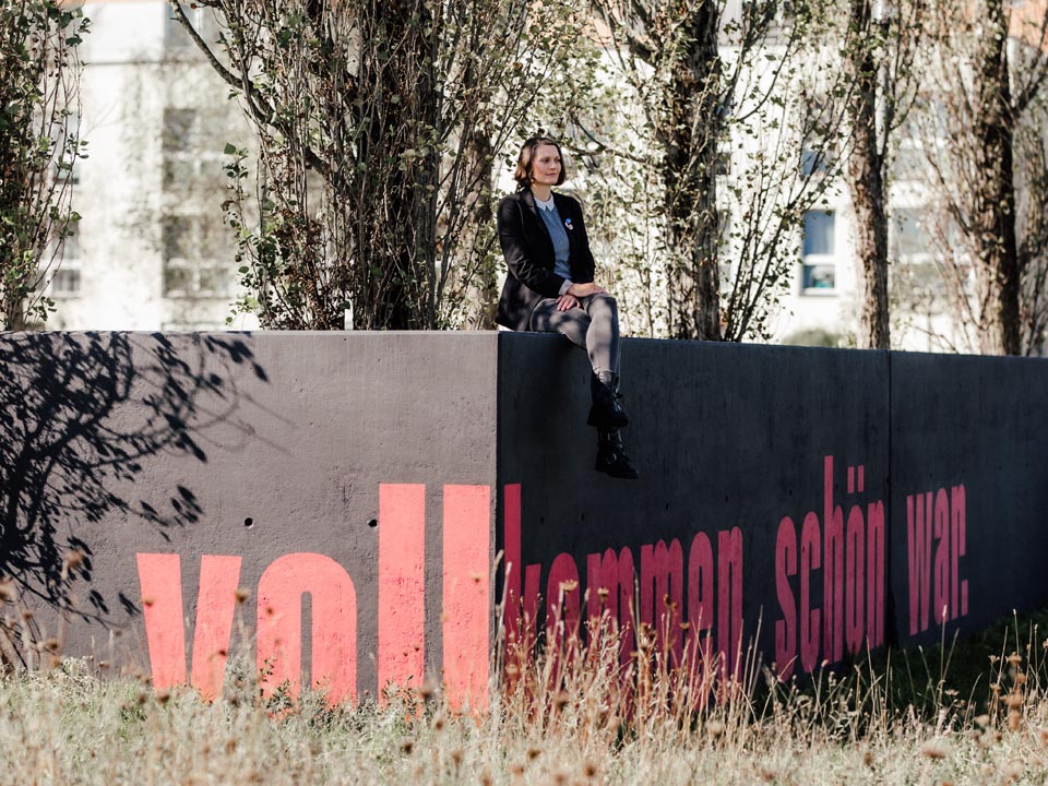 Janina Steger, Philografina, auf einer Mauer sitzend, auf der Mauer der Text "vollkommen schön war" zu lesen