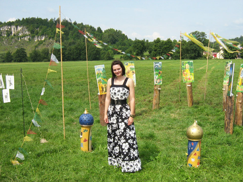 Aufnahme von Janina Steger vor ihren Bildern auf einer Wiese vor Kallmünz im Rahmen der Ausstellung "Ein Fluss verbindet"